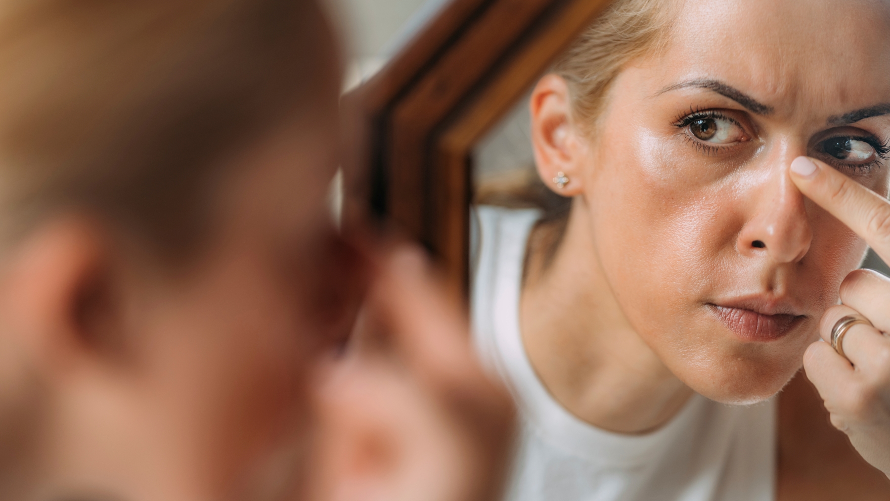 Woman frowning as she looks at face in mirror