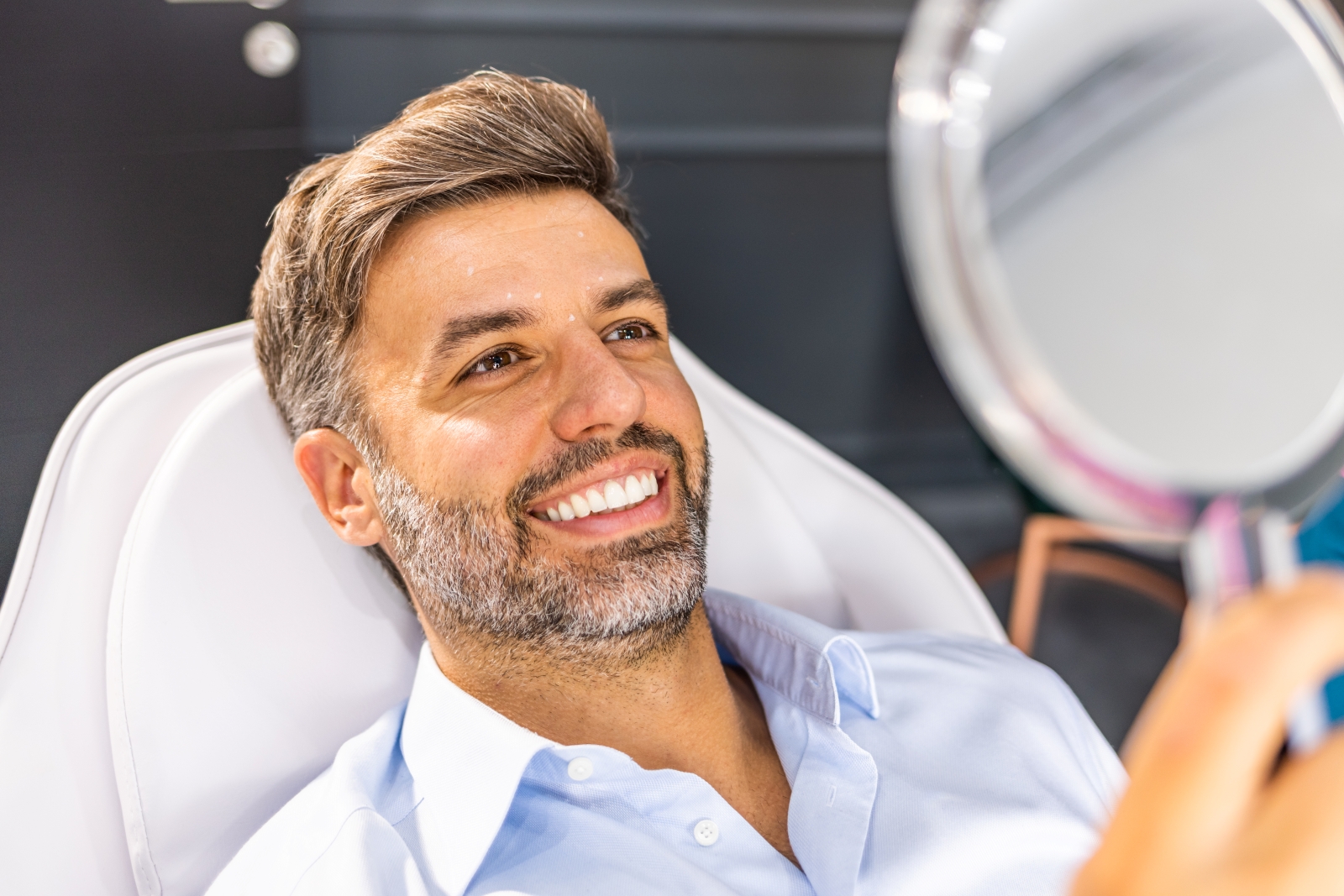 Man smiling and looking at face in hand mirror