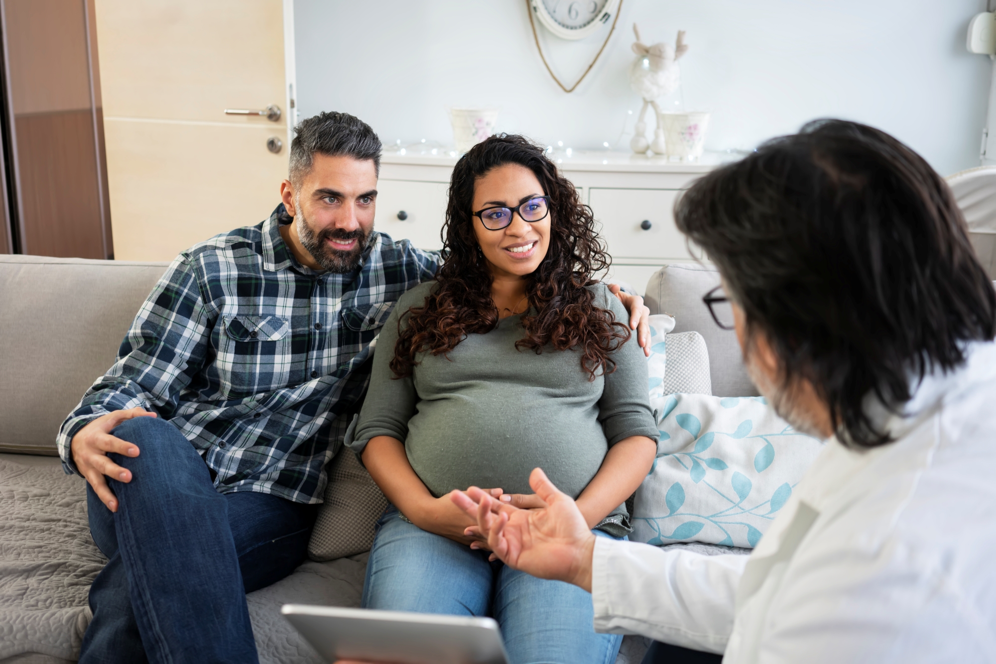 A man has his arm around woman who is pregnant while they speak with physician