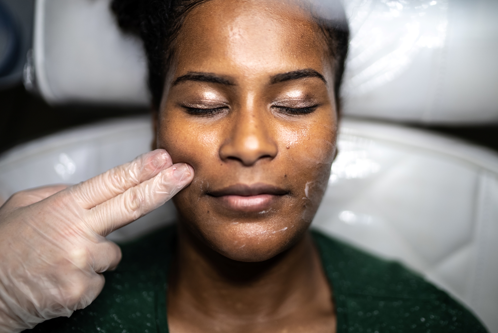Woman with eyes closed before facial treatment with two fingers on gloved hand touching face