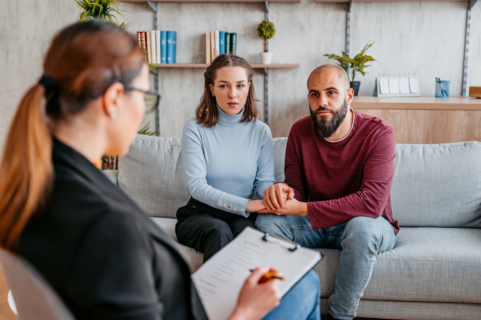 Couple holding hands on sofa while talking with genetic counselor holding clipboard