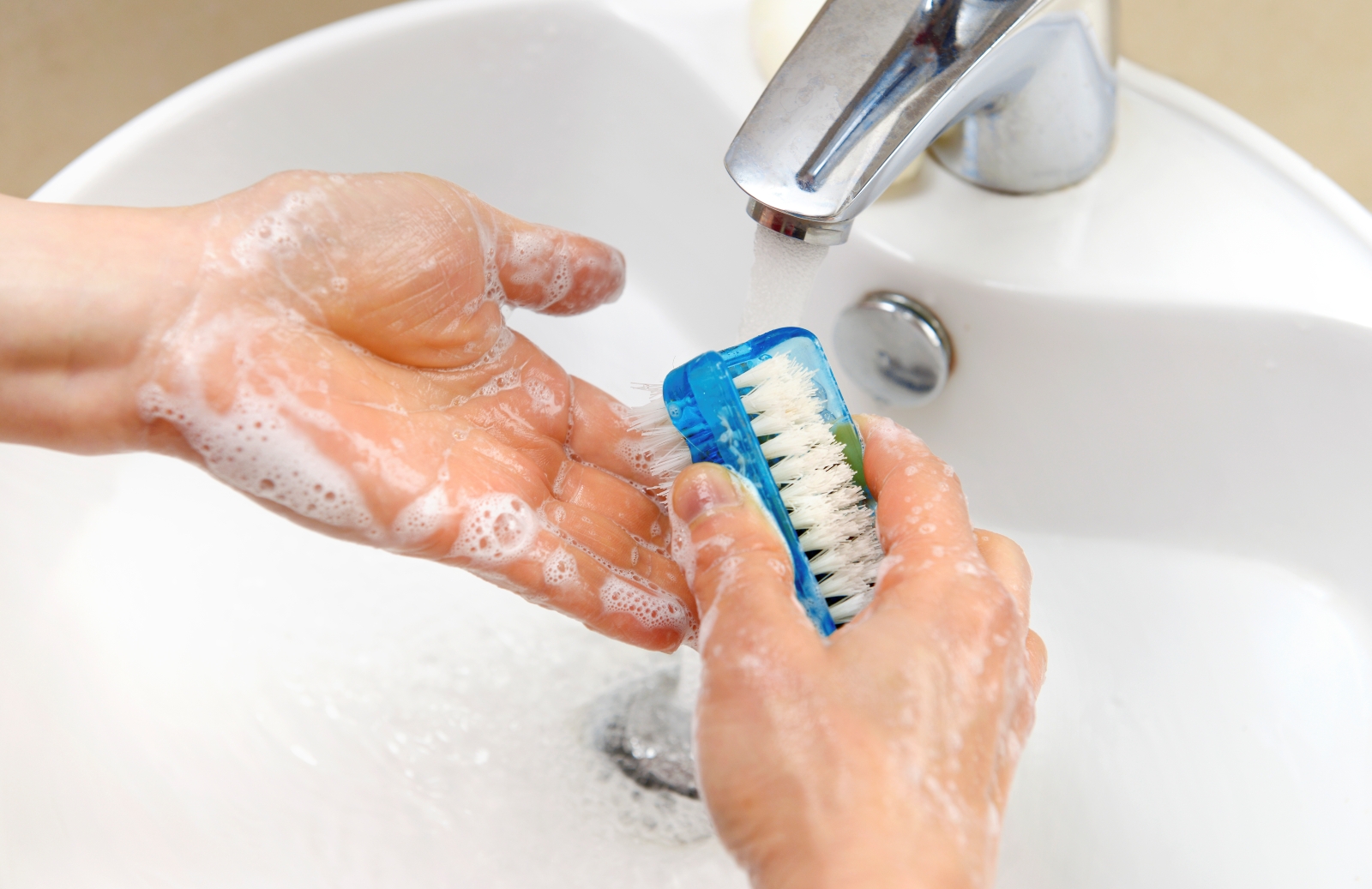 Person washing hands at sink with scrub brush