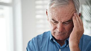 An older man holds his head, looking stressed or in pain.