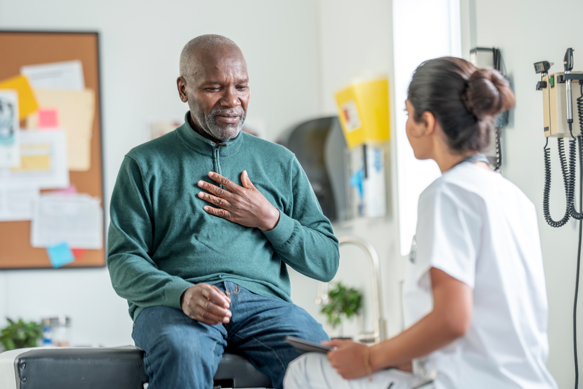 Patient seated at exam table with hand pressed to chest while talking with physician