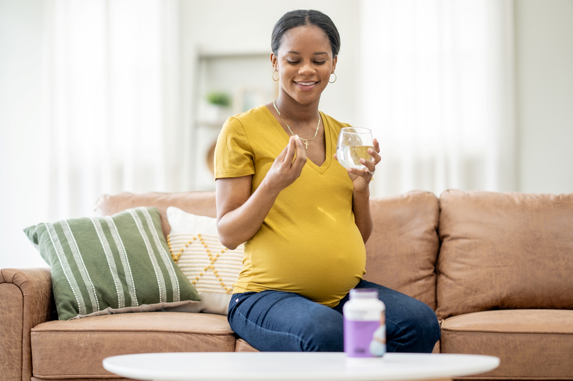 Woman who is pregnant and seated on couch taking a supplement