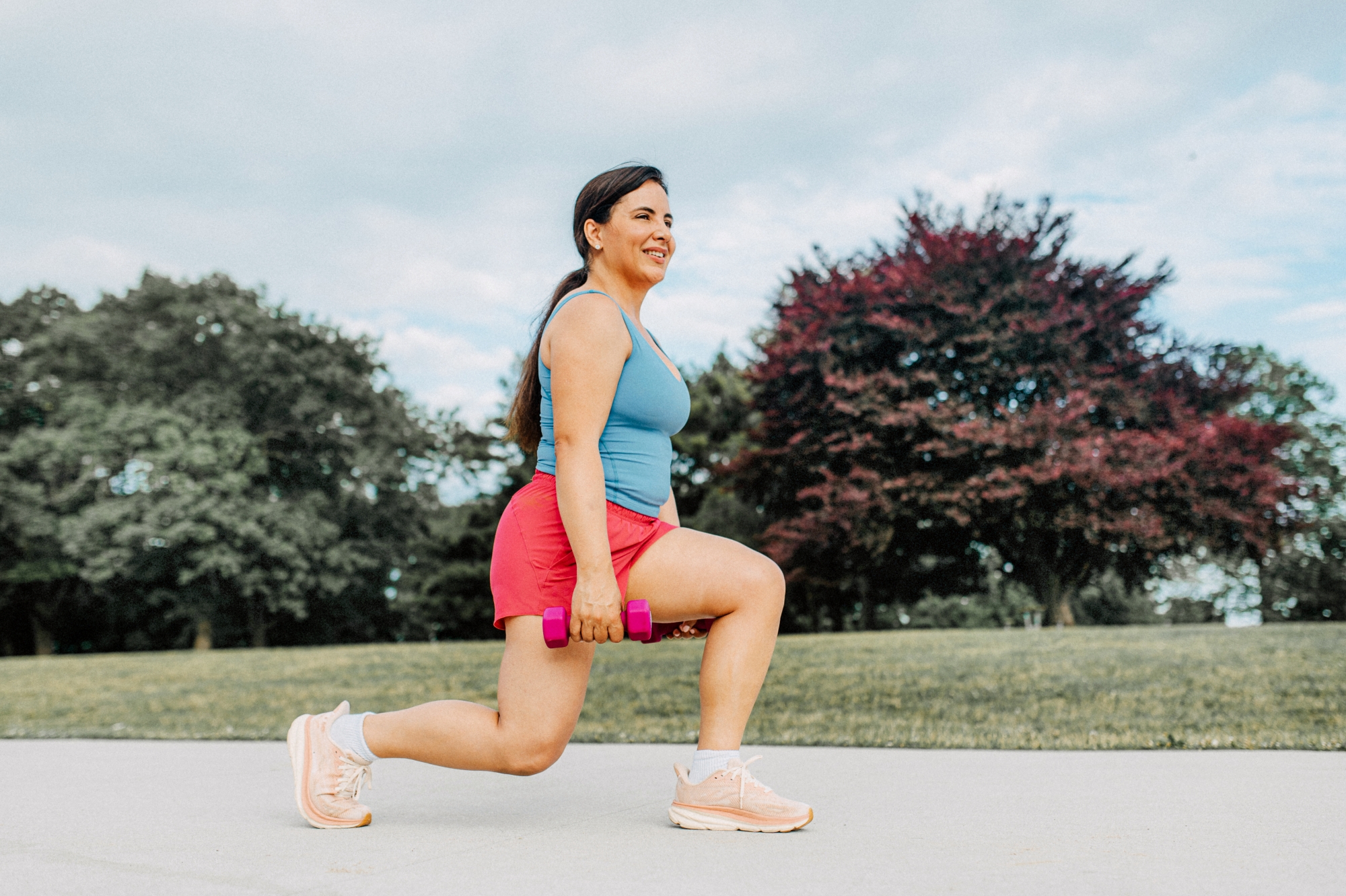 Woman with hand weights doing knee lunges outdoors on cement path