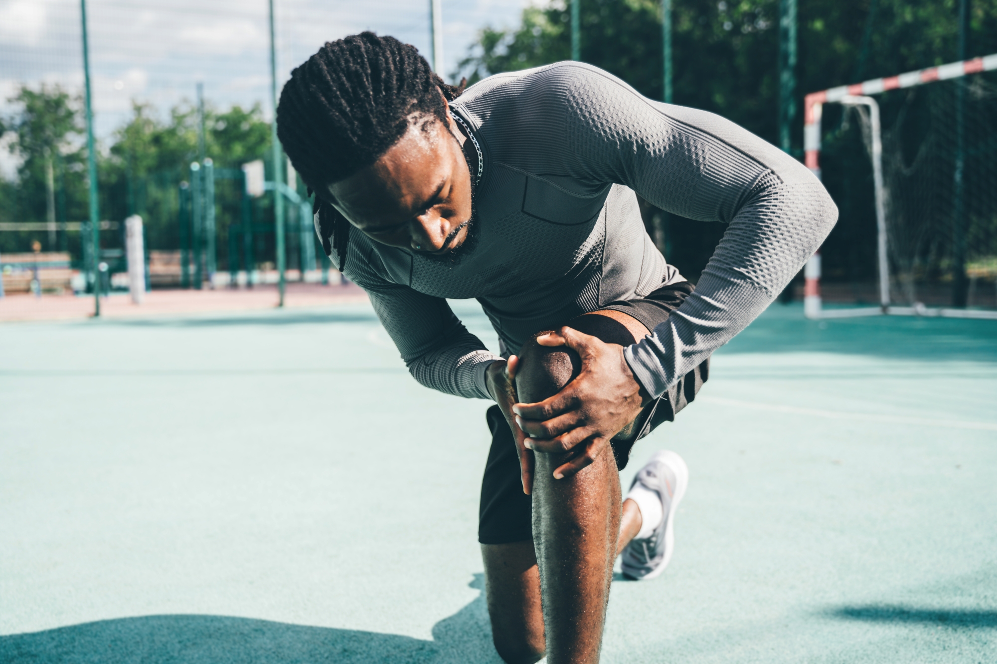 Man on outdoor court kneeling and holding left knee