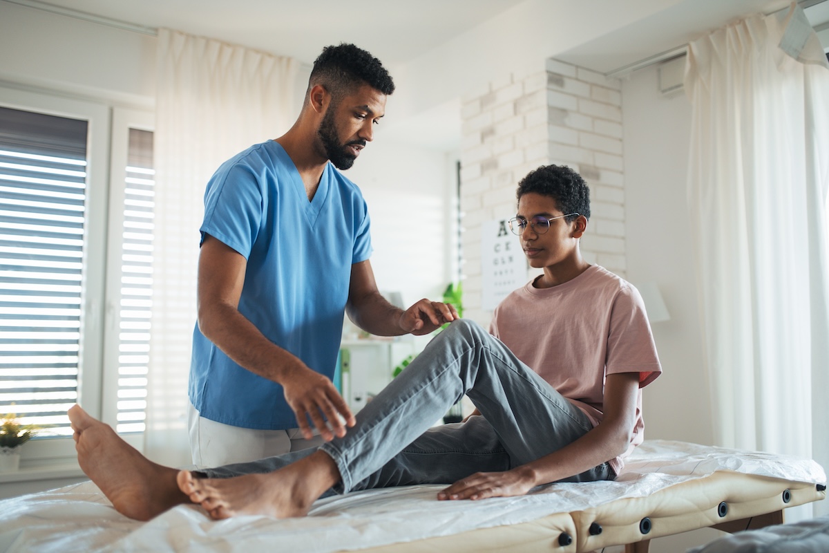 Physical therapist helping a teen with his knee