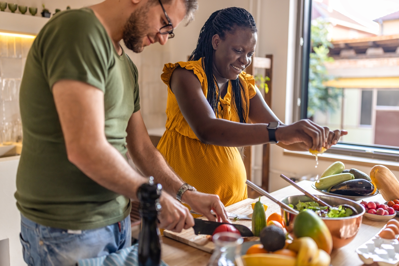Man and pregnant woman preparing food in kitchen