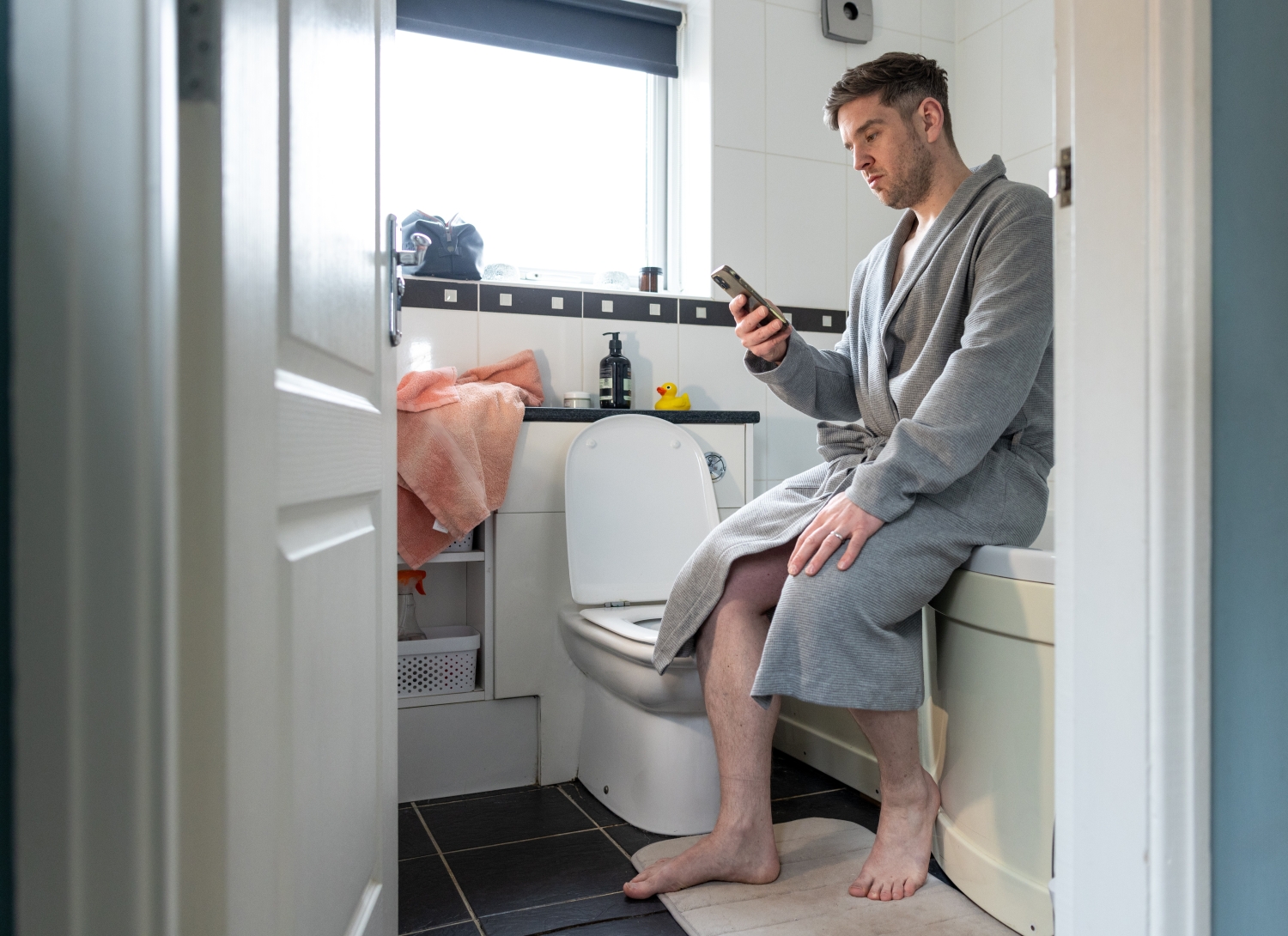 man wearing bathrobe in bathroom while checking smartphone