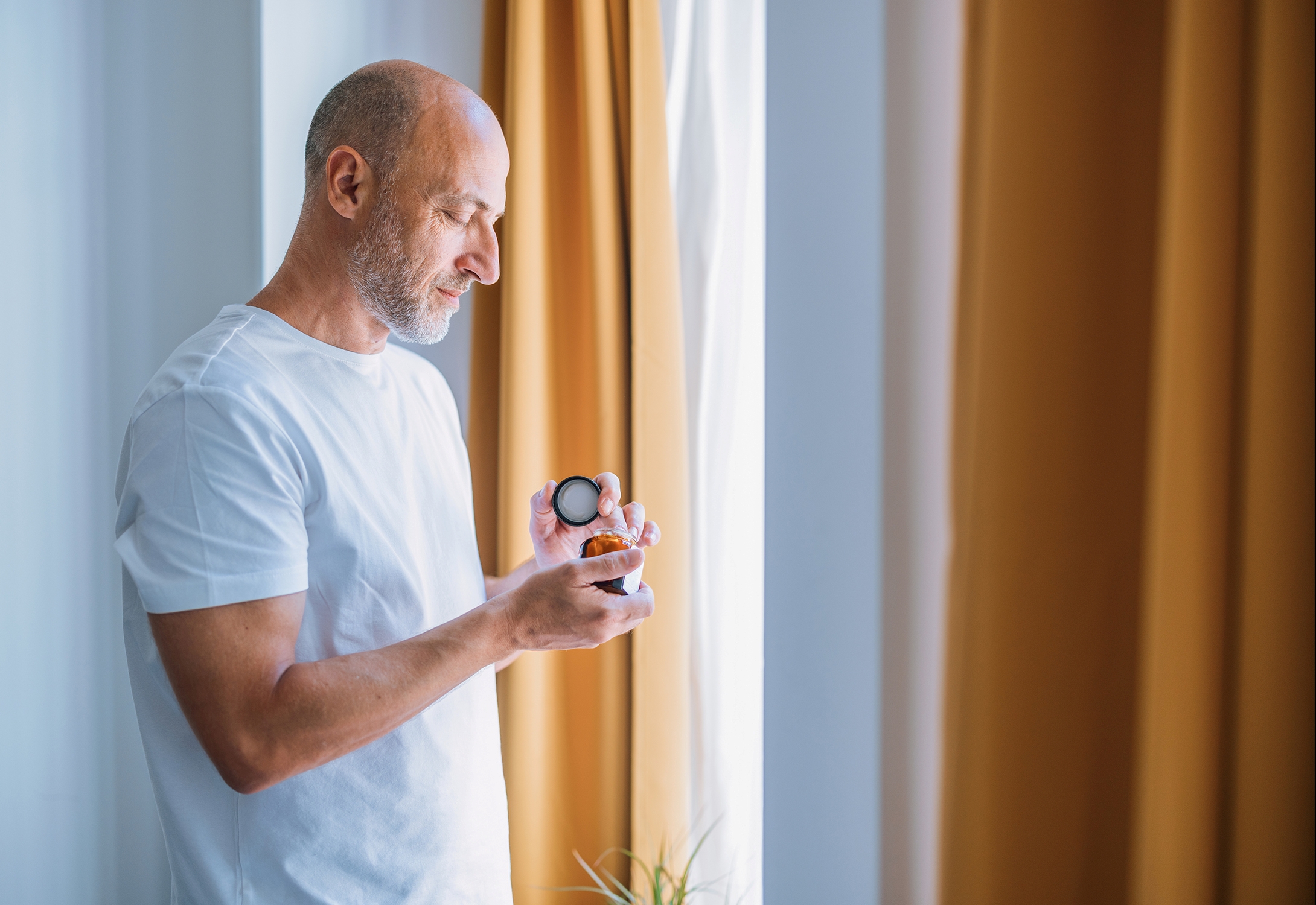 Man standing in front of curtain shakes a pill out of a bottle