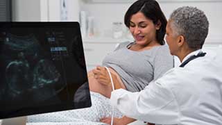 A doctor is performing an ultrasound on a pregnant woman, with the ultrasound image displayed on a monitor nearby.