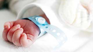 A close-up of a newborn baby's hand wearing a blue hospital wristband.