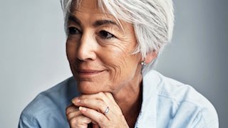 A woman with gray hair with her chin resting on her hands, smiling slightly.