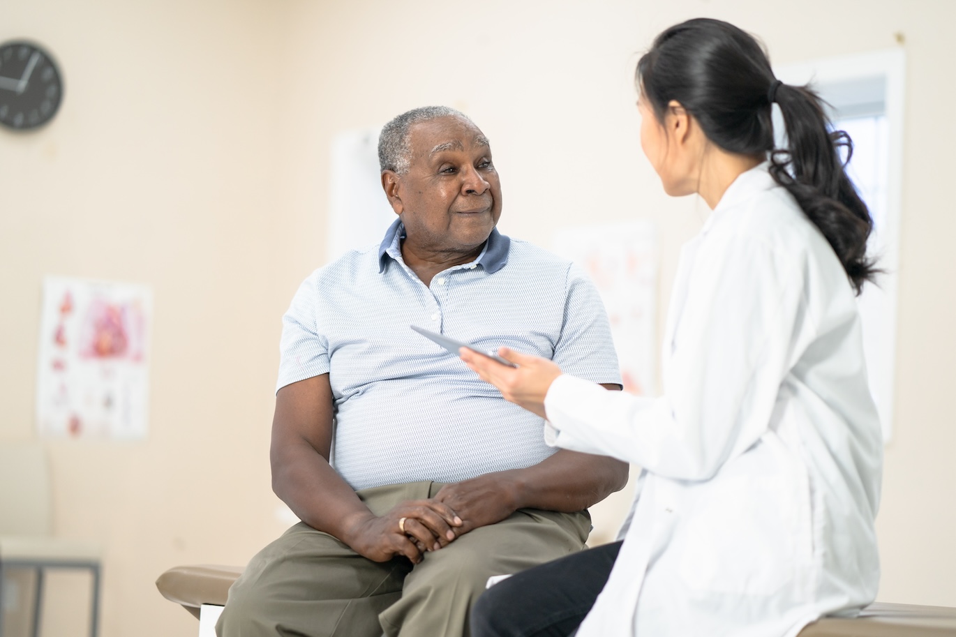 elderly male patient speaking with a female doctor in her office.