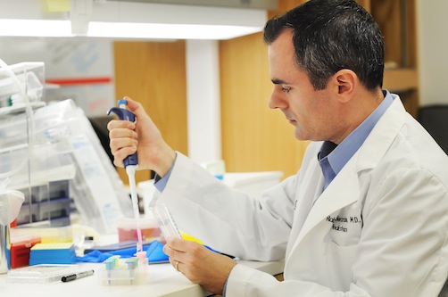 Pediatrician Ralph DeBerardinis, M.D., Ph.D., in a white coat is using a pipette to carefully transfer liquid in a laboratory setting.