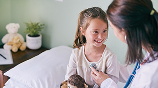 A young girl is smiling while a healthcare professional uses a stethoscope to check her.