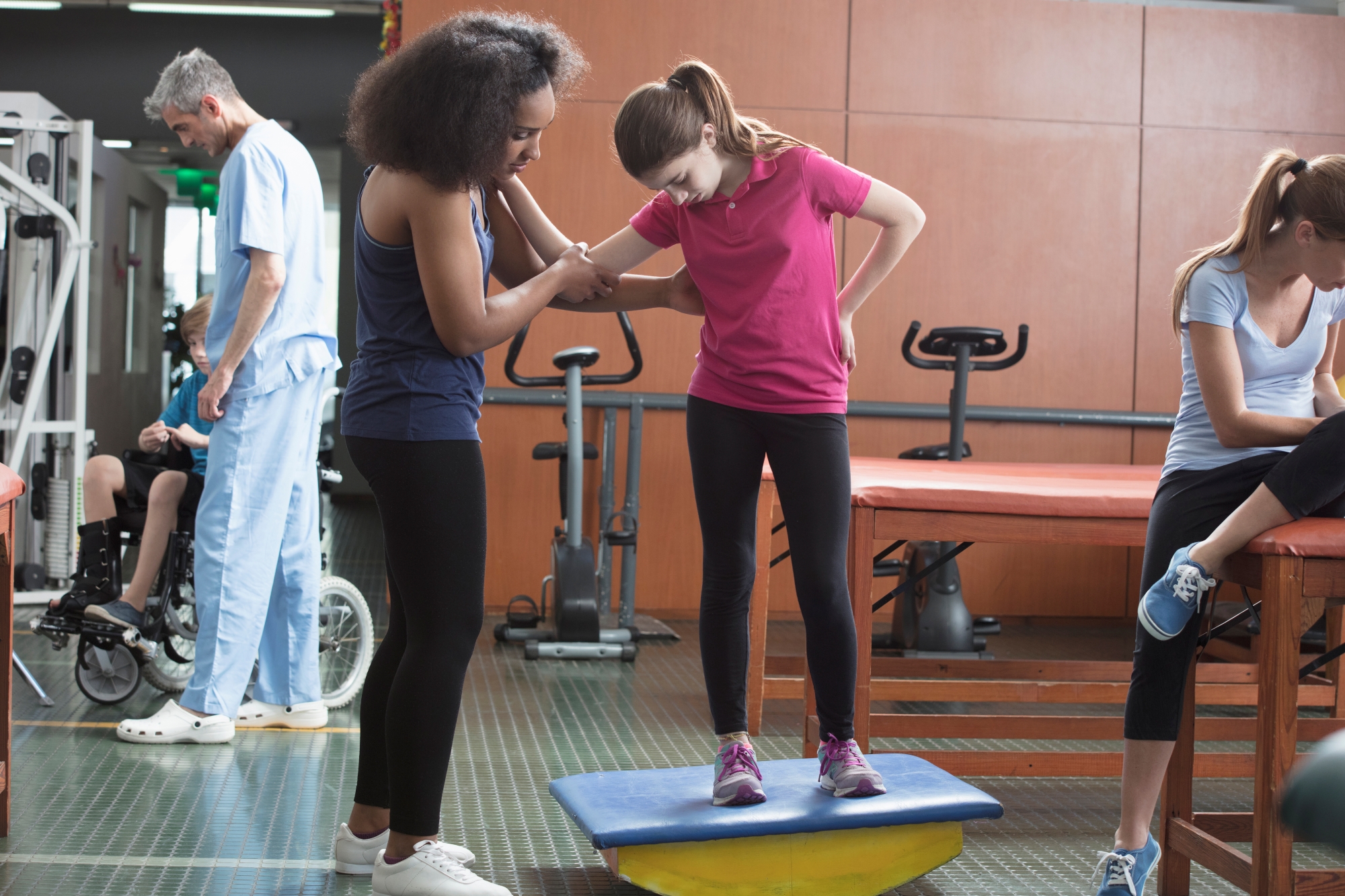 Physical therapist helping female patient balance on rocking platform during PT session