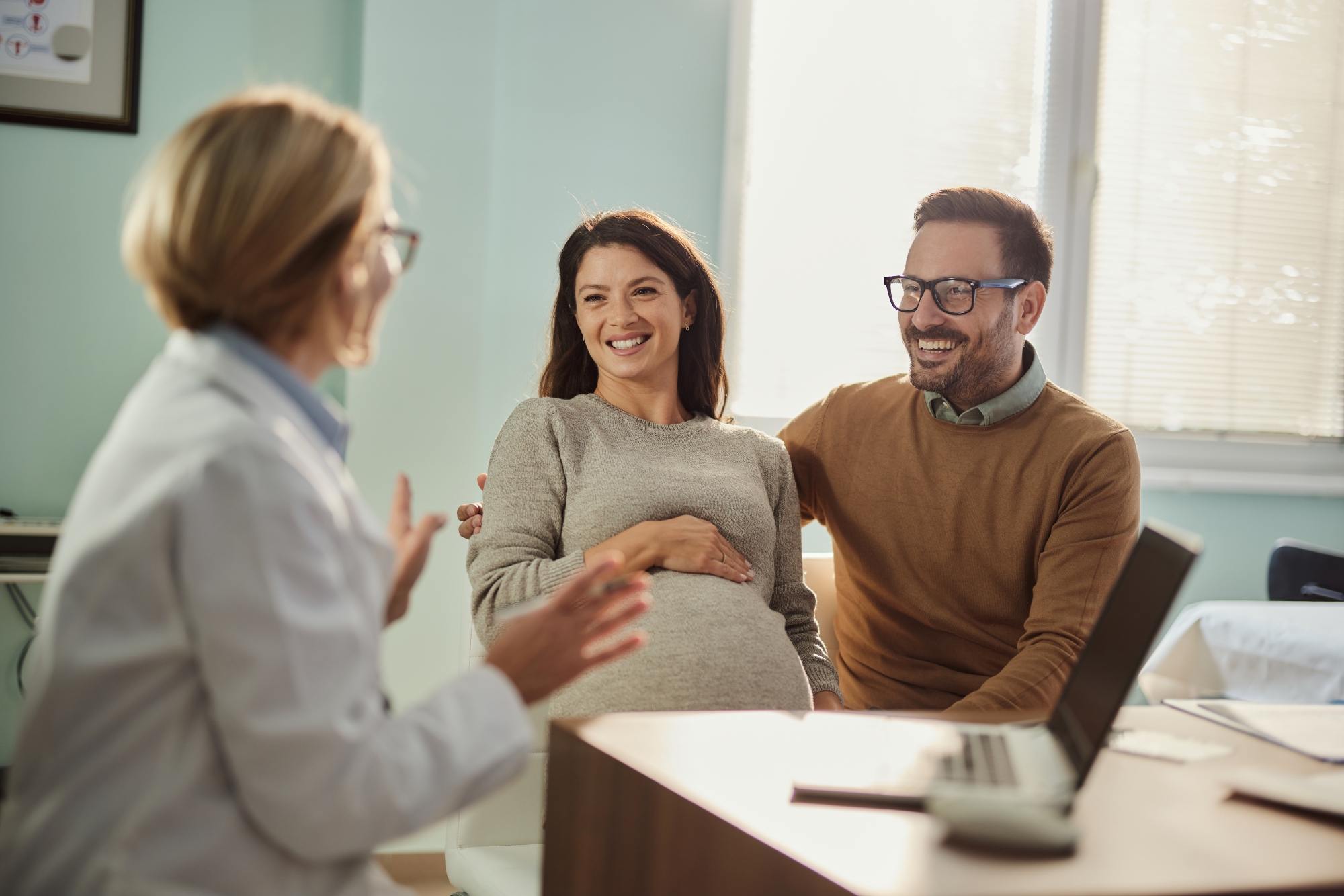 Pregnant woman seated next to man while they talk to a doctor