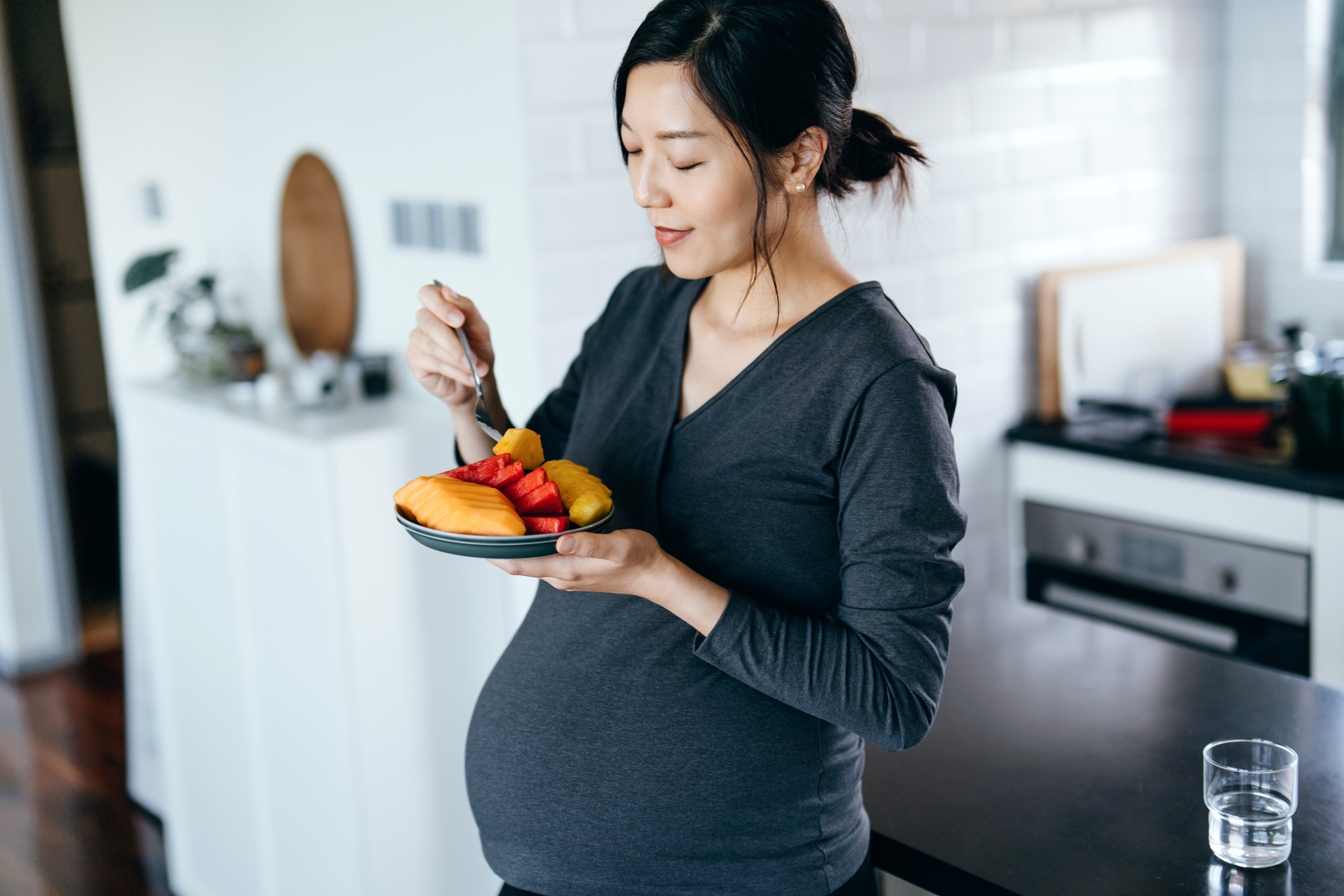A woman who is pregnant and standing while eating food on plate