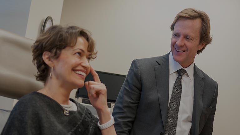 A woman smiling and touching her face while Dr. Jeffrey Kenkel looks on smiling.