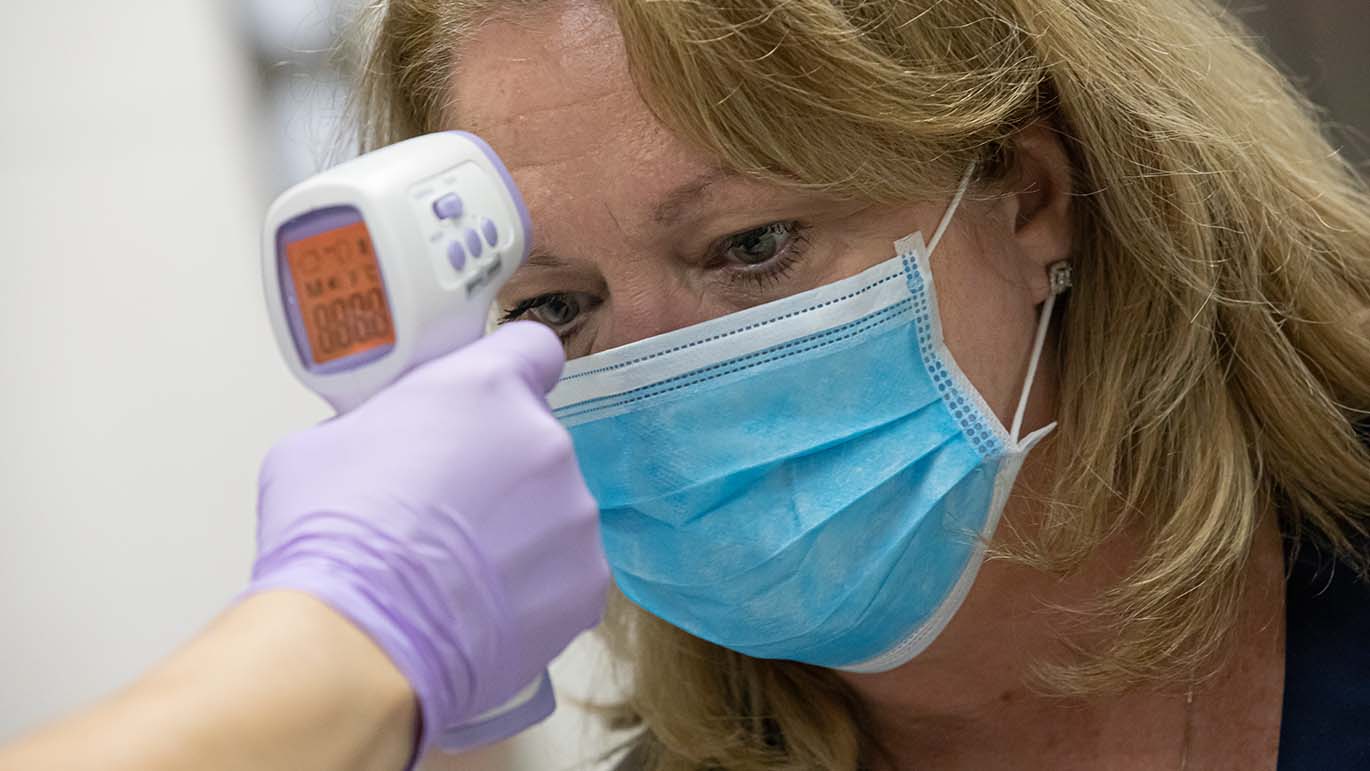 Female wearing a fask mask getting her temperature checked before being admitted.