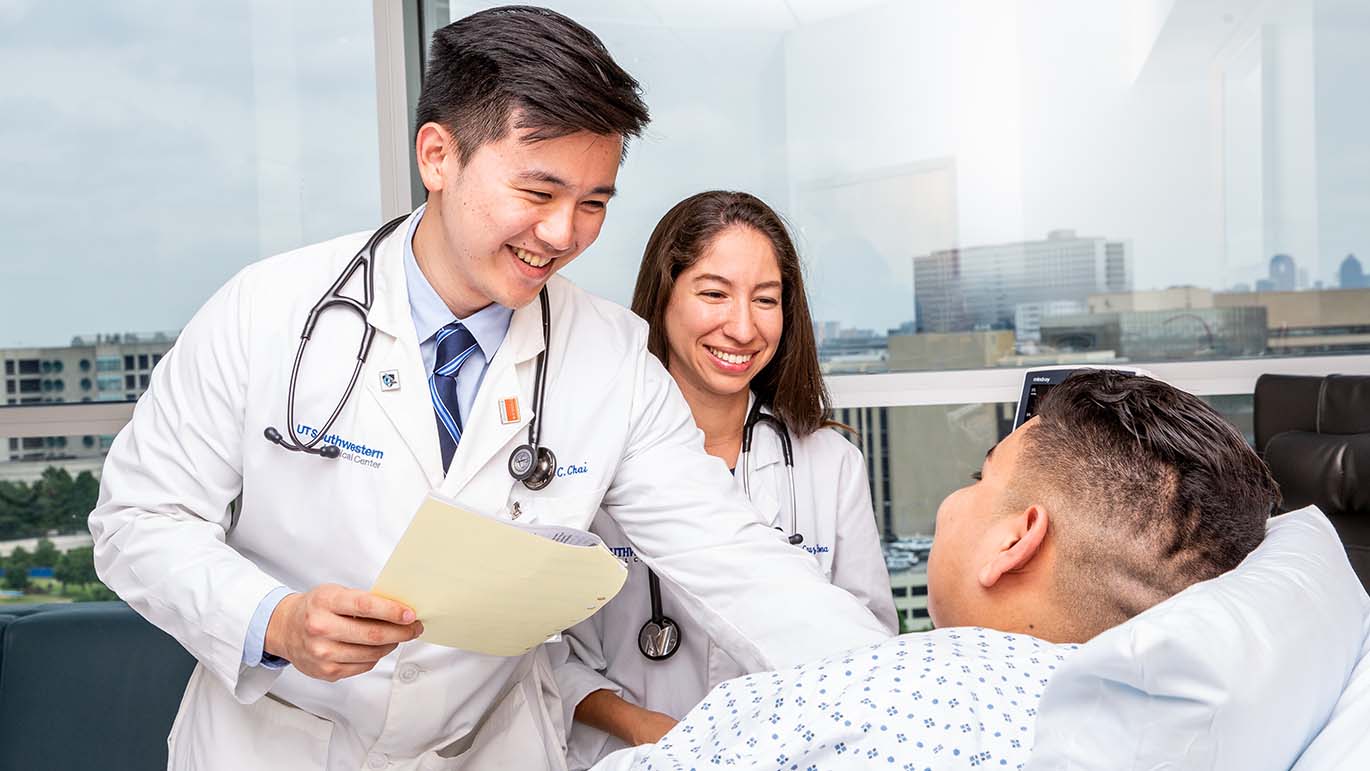 Two doctors smiling and chatting with a patient in a hospital bed.