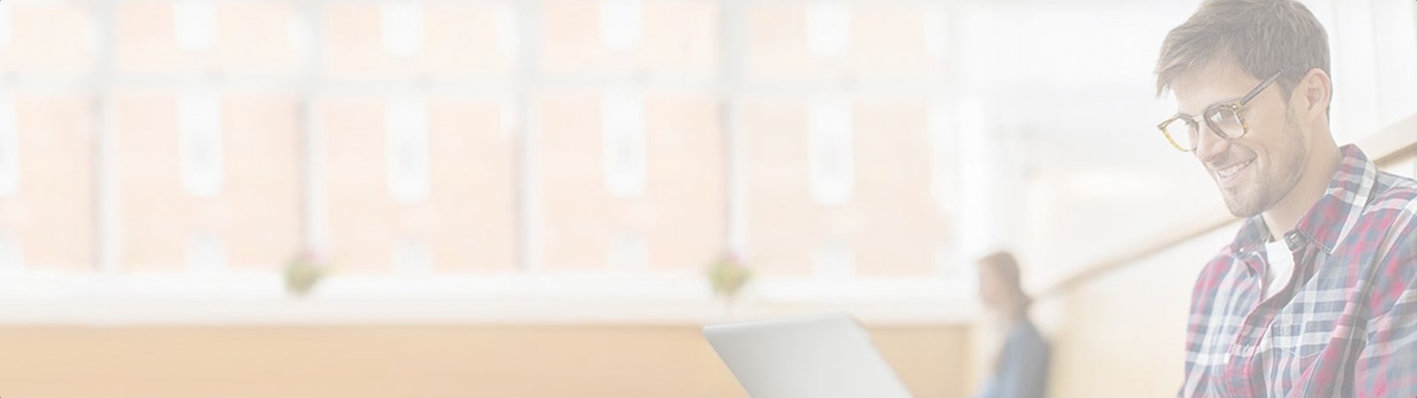 A man sitting in a bright, modern setting, smiling and looking at his laptop.