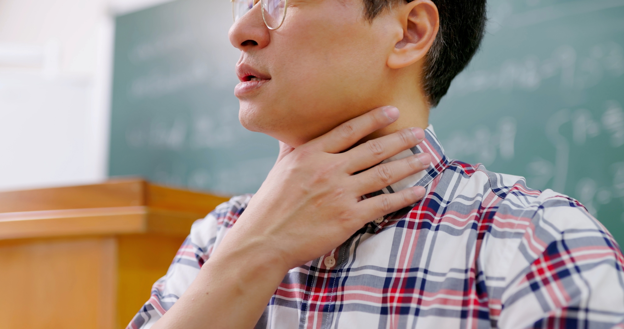 a male professor in classroom holds sore throat