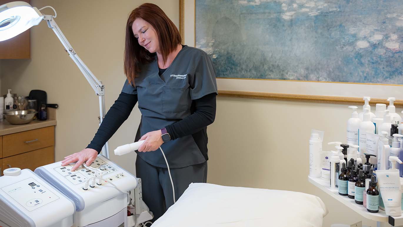 A skincare professional is preparing a treatment device in a well-equipped skincare treatment room, ready for the next client.