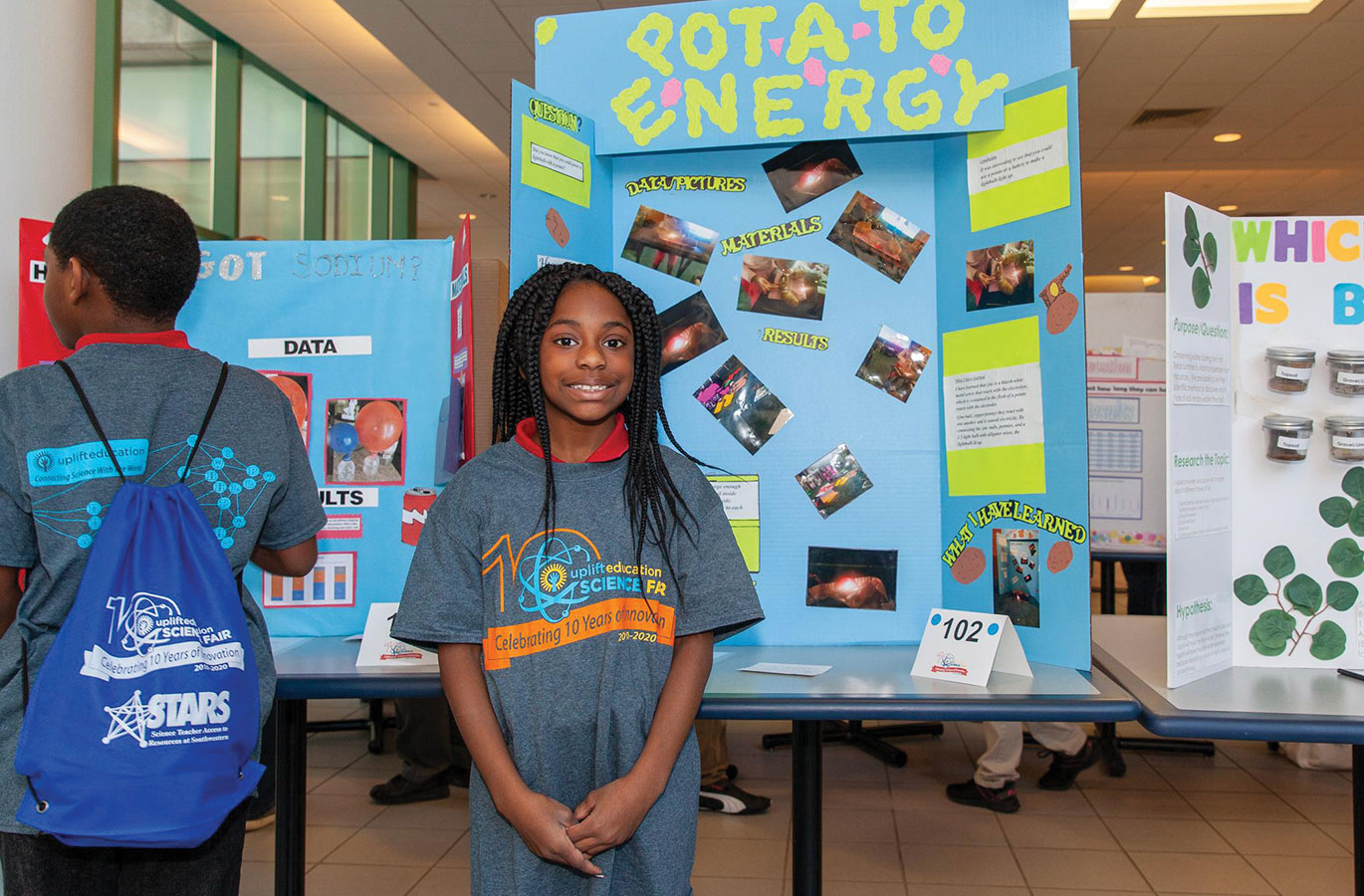 young girl standing in front of a display of science projects at a school science fair