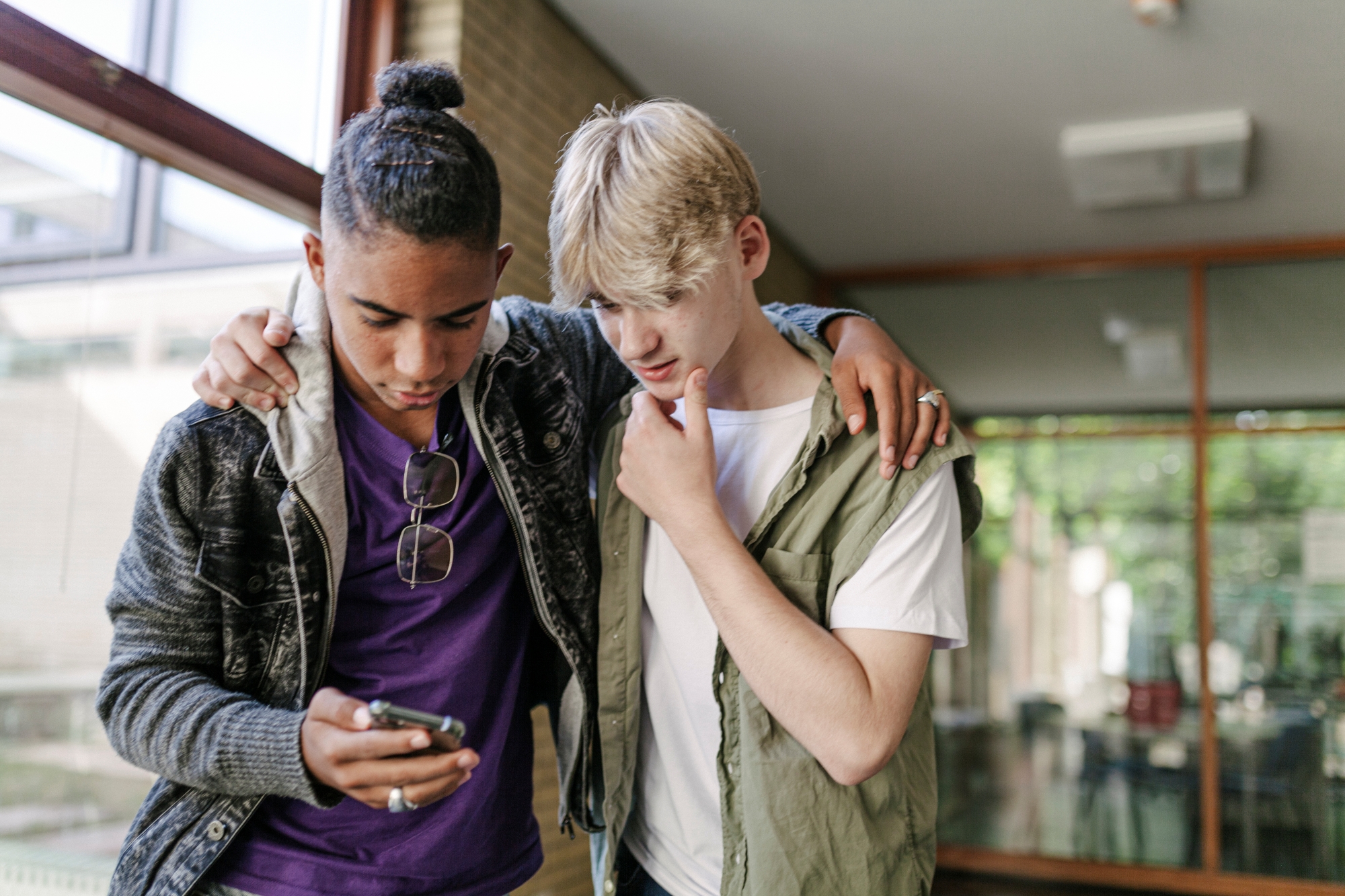 Two teen boys huddled together looking at smartphone