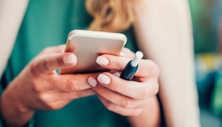 Close-up of a person holding a smartphone and a vaping device
