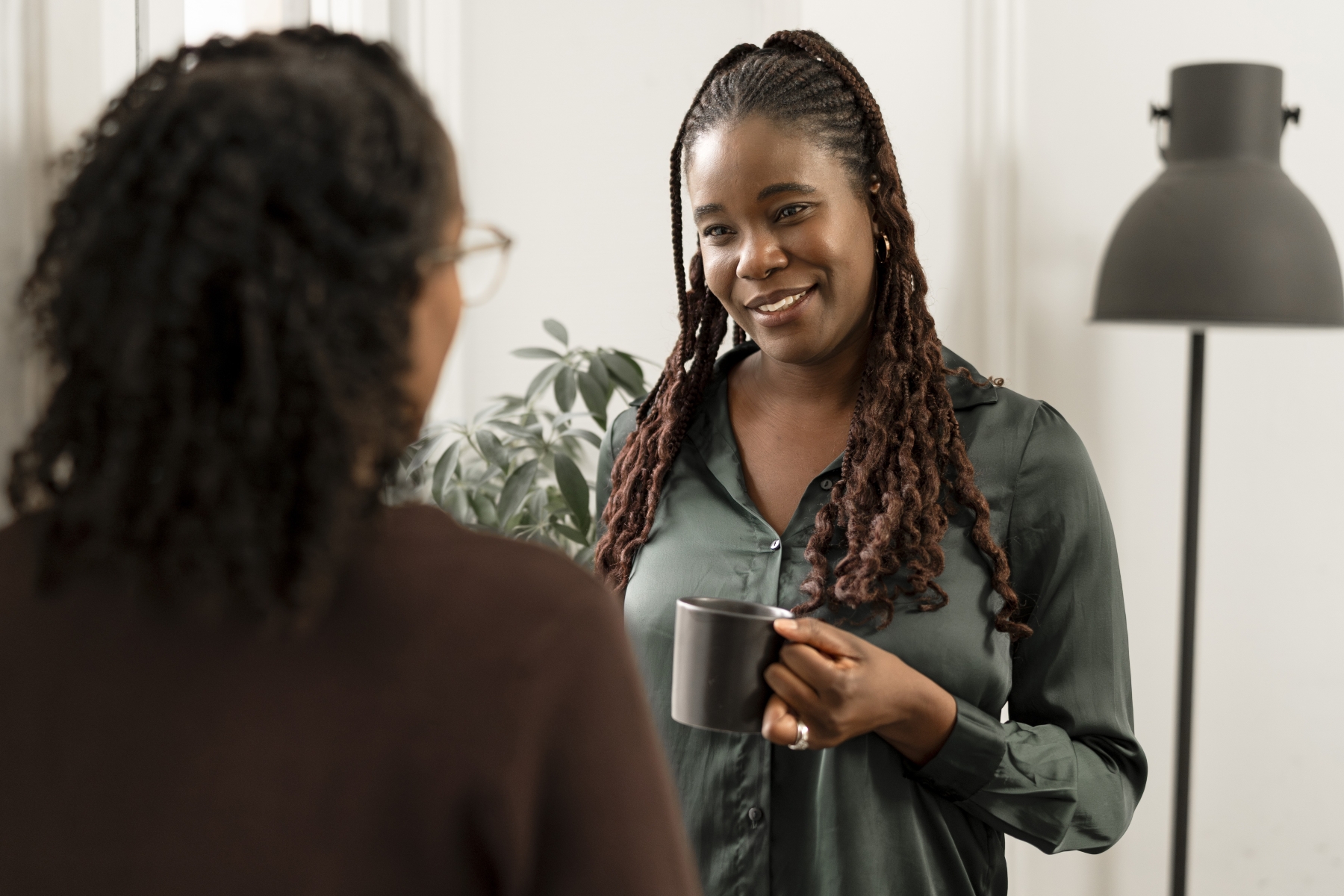 Two women talking with one facing the camera and holding mug and the other with her back to camera